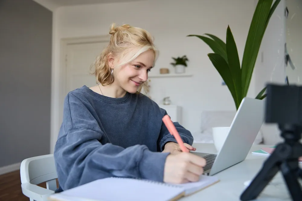 A smiling high school student studying on a laptop, representing the online A-level Business course at ATMO School